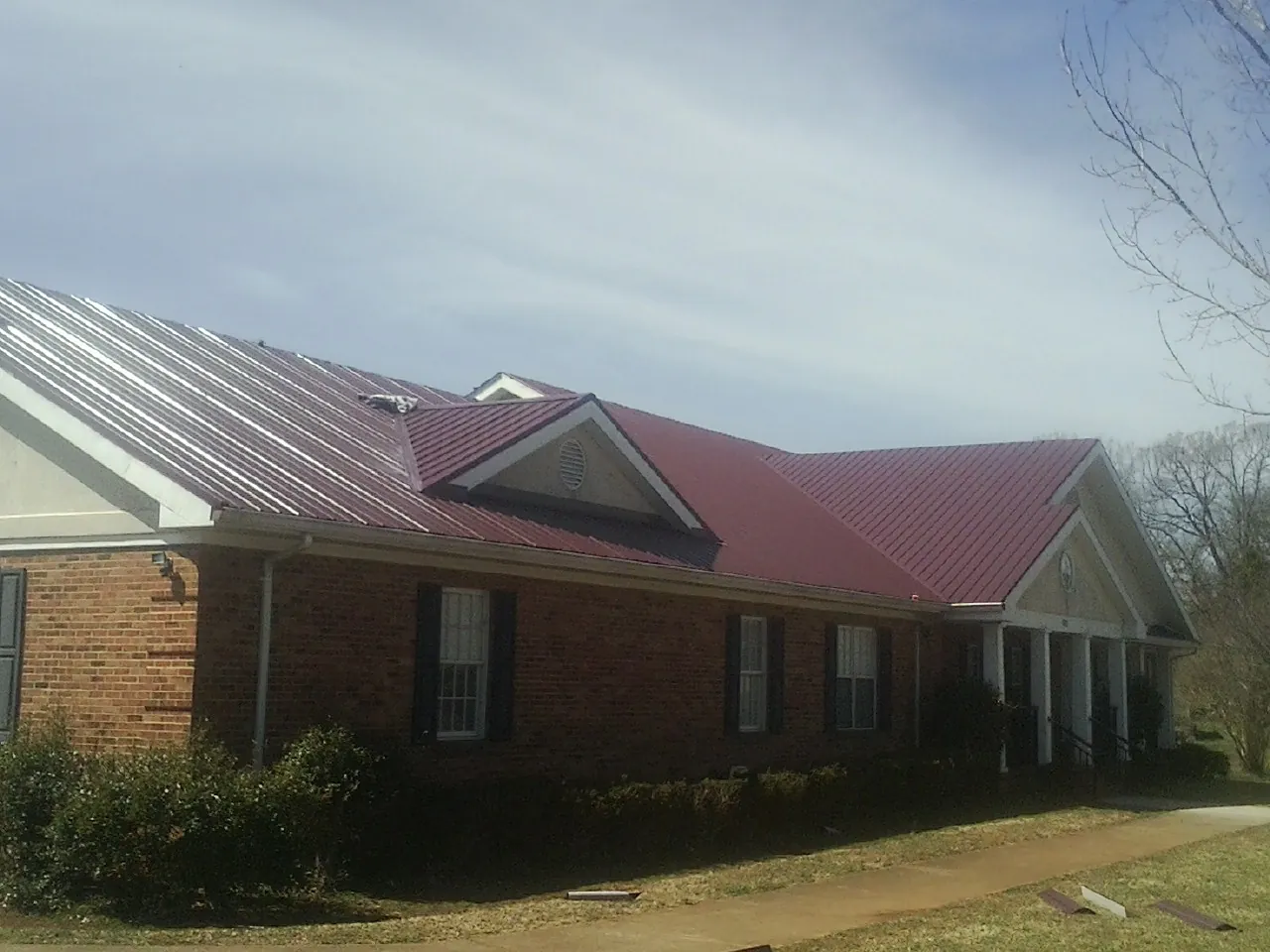 Red metal roof with gabled entries on a long brick building, from a Hail Damage Roof Repair job in Poulsbo
