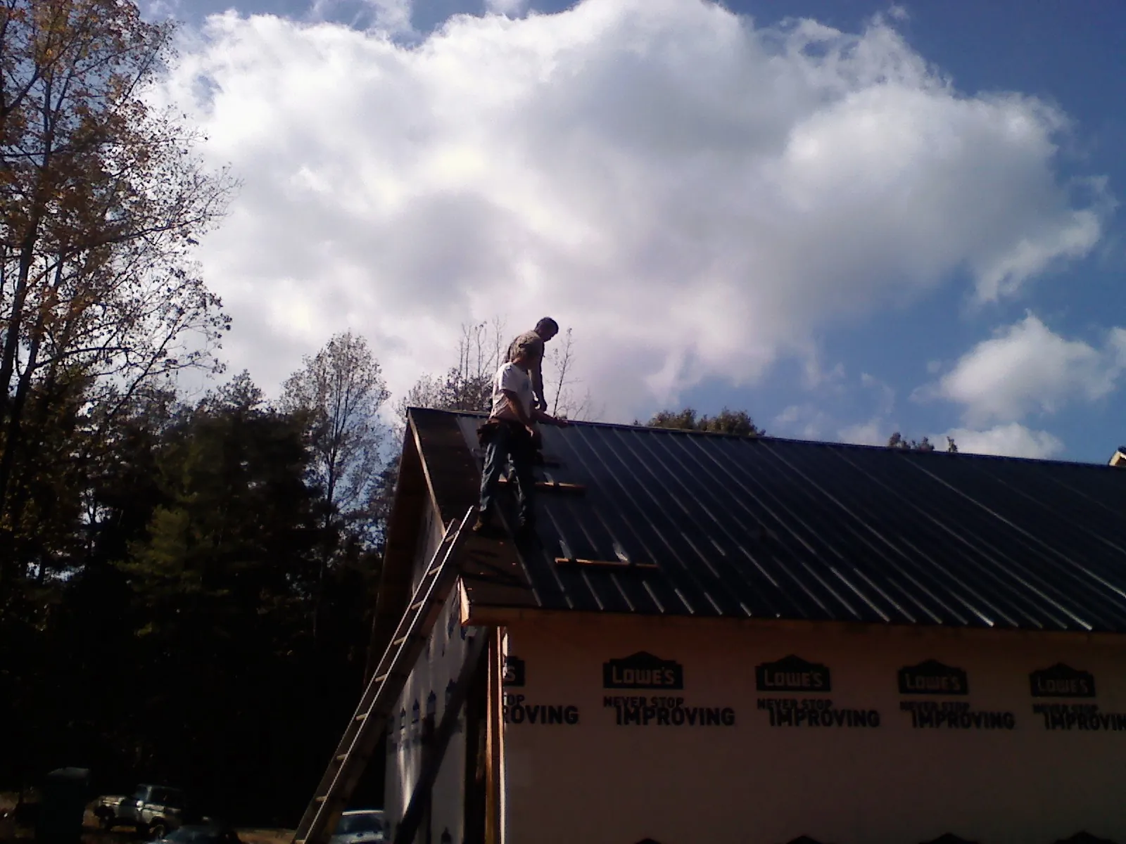 Roofer fastening dark metal panels high against a cloudy sky, from a Roof Inspection job in Poulsbo