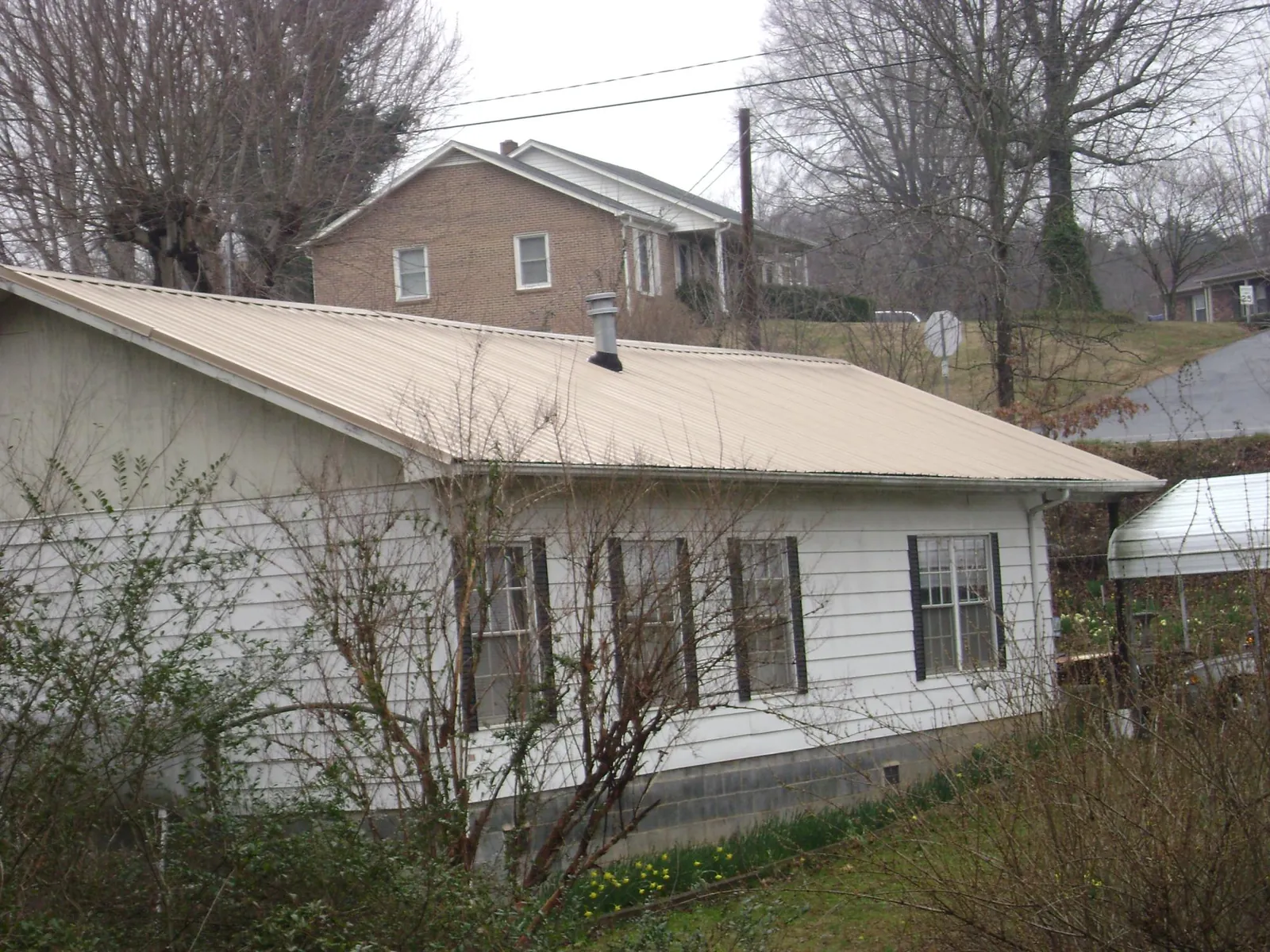 Tan metal roof on a white sided house set into a hillside — Commercial Roofing by Roofing Brothers in Poulsbo